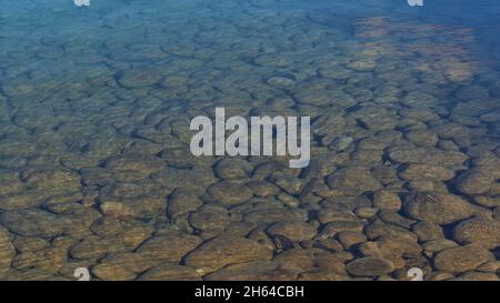 Shimmering water surface on the shore of Lake Beauvert in Jasper, Alberta, Canada in the Rocky Mountains with round stones in the sunlight in autumn. Stock Photo