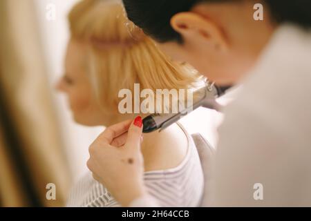 Hairdresser makes the girl styling with a curling iron. Close-up. Side view Stock Photo