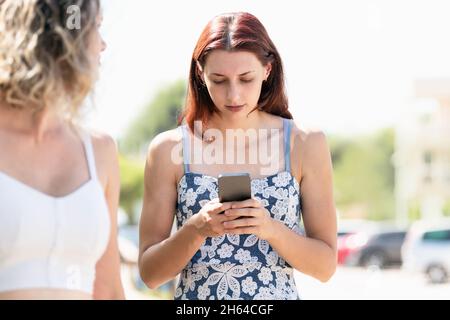 Concentrated woman using a mobile while standing next to a friend Stock Photo