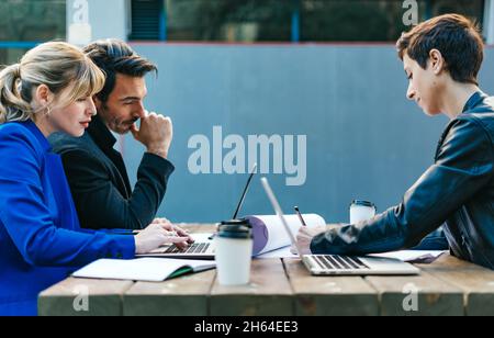 Group of corporate colleagues working together outdoors. Modern business professionals having a discussion during coffee break. Stock Photo