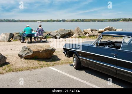 Greenwich, CT, USA-May 2011; View of a classic Chevrolet Impala seen from the side with two people in front of car on a bench Stock Photo