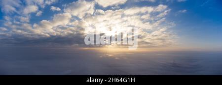 Sunrise in the clouds over a thick fog. Panorama of the morning sky shot high from a drone. Stock Photo