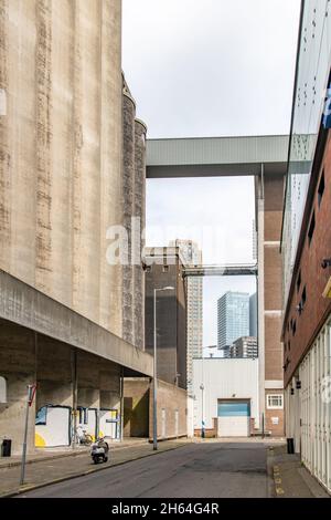 Rotterdam, the Netherlands-July 2021; View through desolate street between warehouses and grain elevator silos in urban area with skybridge Stock Photo
