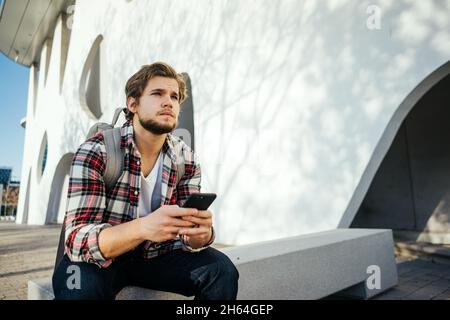 Portrait of modern young man with smartphone on a street. Hipster guy with mobile in his hand outdoors Stock Photo
