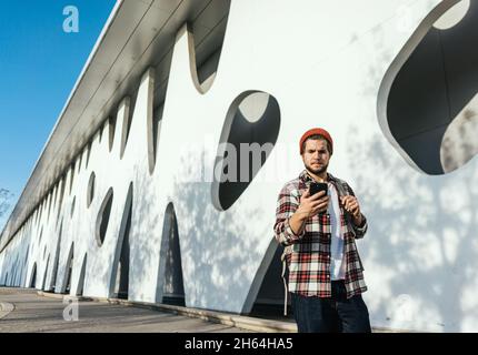 Portrait of modern young man with smartphone walking down the street. Hipster guy with mobile in his hand outdoors Stock Photo