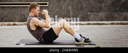 Picture of a fit young man doing crunches. Athlete doing fitness training outdoors. Workout during lockdown outside the gym. Stock Photo