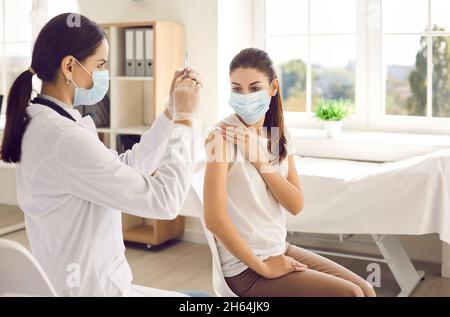 Nurse preparing syringe to give injection of vaccine to female patient at vaccination center. Stock Photo