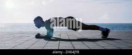 Fit young man doing plank on seafront. Fitness training in morning outdoors. Workout during lockdown outside the gym. Stock Photo