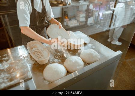 Baker covers inner surface of dish for bread with flour in workshop Stock Photo