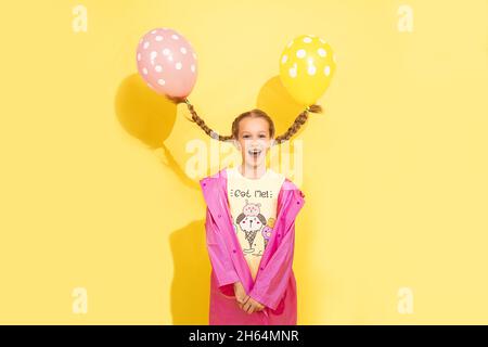 funny little pretty girl flies away on balloons tied to 2 pigtails. concept of magic, fantasy, humor, children's party. Positive emotions of surprise, Stock Photo