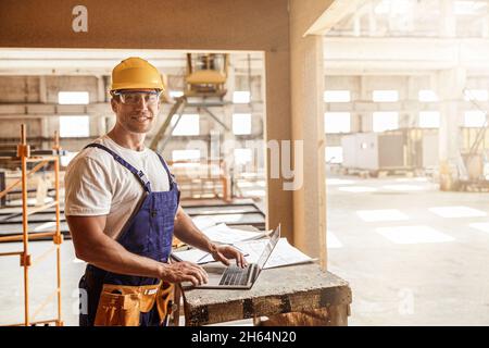 Cheerful male builder using laptop at construction site Stock Photo