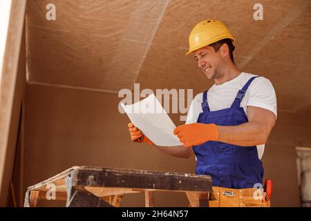 Joyful builder studying architectural plan at construction site Stock Photo