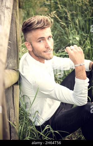 Blondish, blue eyed young man on wood fence Stock Photo