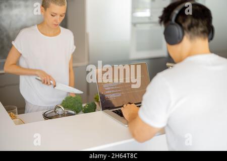Woman cooking dish while man using laptop Stock Photo