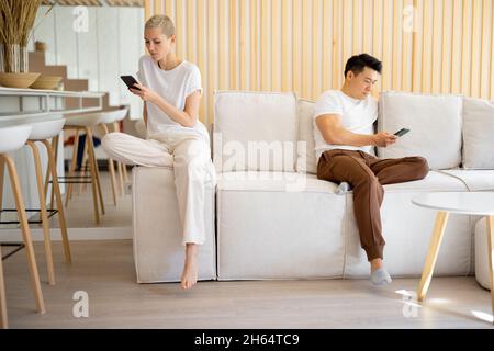 Couple using smartphones on sofa at home Stock Photo