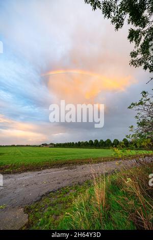 Bright colorful part of a rainbow over a country road in the fields Stock Photo