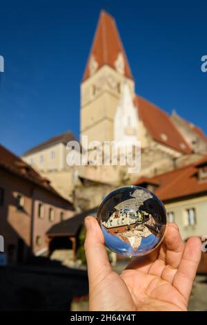 Hand holding glass sphere in front of old church in Weissenkirchen, Wachau (Austria), sunny day in autumn Stock Photo