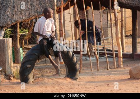 A young boy sits on a disused tyre now being used as a resting place at a Selous growth point. Old tyres have a variety of uses in Zimbabwe, including making shoes and furniture. Zimbabwe. Stock Photo