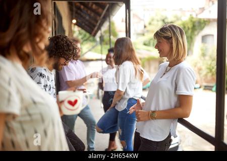 group of young adult people having a break at work, standing outdoor, smoking cigarettes, drinking coffee, talking, smiling Stock Photo