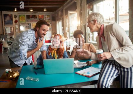 An elderly female boss in a cheerful atmosphere in the office is having a good time while working with her young colleagues Stock Photo