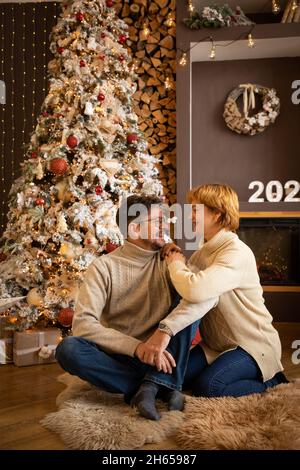 Couple sitting on the background of Christmas tree at home, Happy New Year 2022 Stock Photo