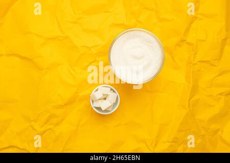 Sugar in glass bowl on yellow background. Diabetes and unhealthy diet concept. Top view, flat lay, copy space. Stock Photo