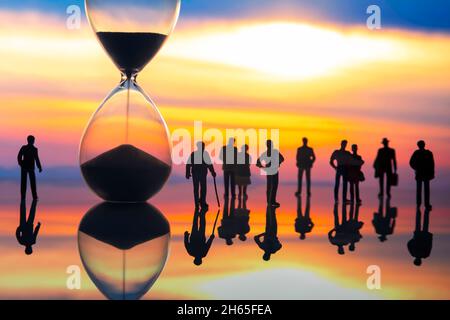 miniature people. silhouettes of different people watching the sunset next to the hourglass. end of life. Stock Photo