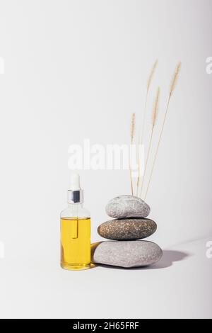 Spa composition with bottle of organic cosmetic oil next to stack of stones on white background Stock Photo