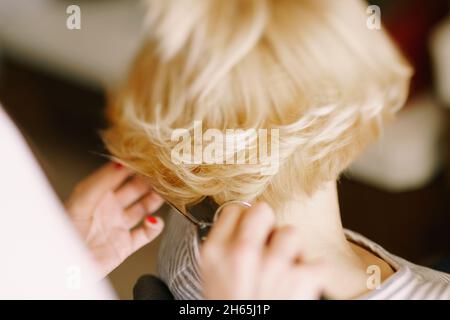 Hairdresser curls the girl's short hair with a curling iron. Close-up. Back view Stock Photo