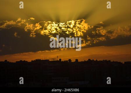 Houses silhouettes with gorgeous sunset sky background. Rays of sun break through clouds. Evening sun setting on row of city houses. Stock Photo