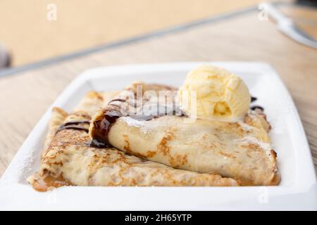 Delicious caramelized condensed milk crepes plate with vanilla ice cream, chocolate and icing sugar. Sweet dessert concept Stock Photo