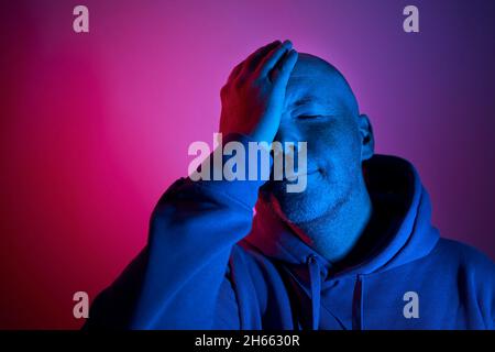 Portrait illuminated of neon lighting. Gesturing middle aged man in purple and blue lights. Stock Photo
