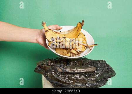 Woman throwing banana peels in trash can. Throw out banana peels in garbage. Banana skin in recycling bio bin in the kitchen Stock Photo