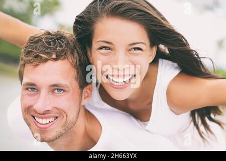 Happy couple having fun piggybacking laughing on summer honeymoon holidays vacation on beach. Beautiful interracial multi-ethnic dating people on Stock Photo
