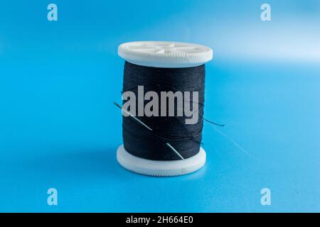 Black thread and needle, close-up photo of black thread isolated on blue background. Stock Photo