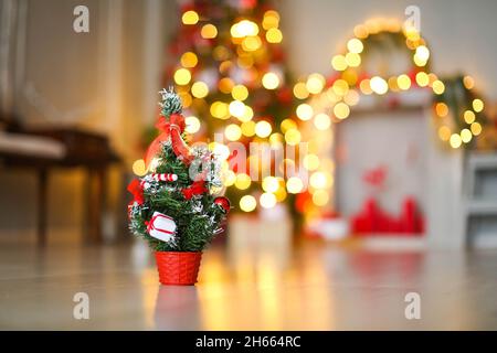 Small artificial Christmas tree on the background of bright yellow garlands and Christmas tree. Stock Photo