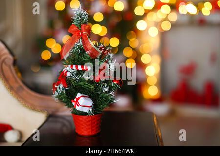 Small artificial Christmas tree on the background of bright yellow garlands and Christmas tree. Stock Photo