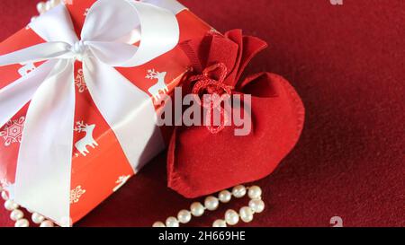 Red gift bag and Christmas gift box, festively decorated with a white ribbon on a red background. Christmas background. Stock Photo