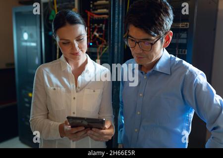 Diverse male and female engineers using digital tablet in computer server room Stock Photo