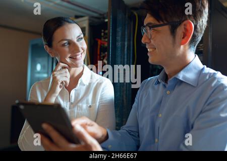 Diverse male and female engineers smiling while using digital tablet in computer server room Stock Photo