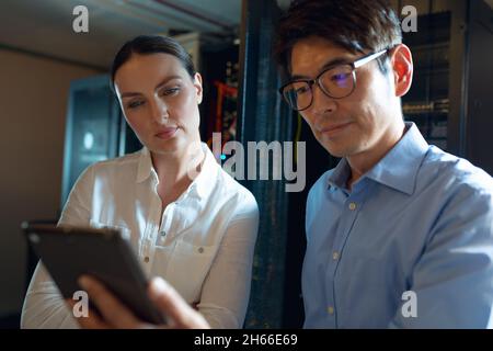 Diverse male and female engineers using digital tablet in computer server room Stock Photo