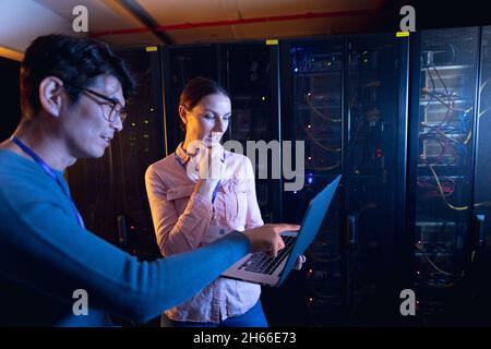 Diverse male and female engineers using laptop in computer server room Stock Photo