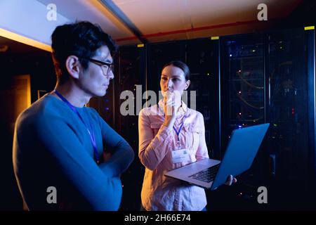 Diverse male and female engineers using laptop in computer server room Stock Photo