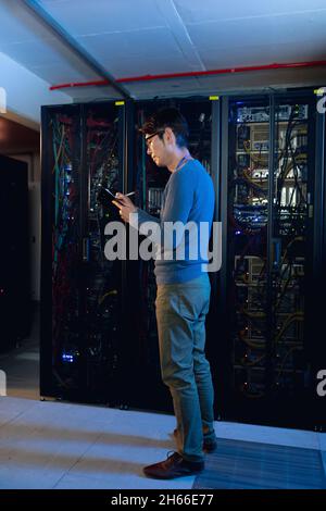 Asian male engineer writing on clipboard in computer server room Stock Photo