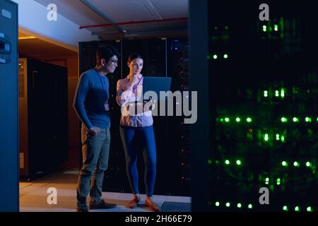 Diverse male and female engineers using laptop in computer server room Stock Photo