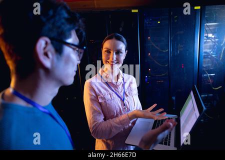 Diverse male and female engineers using laptop in computer server room Stock Photo