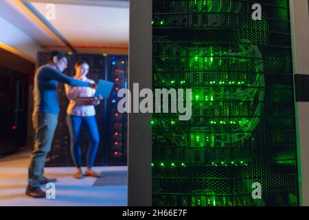 Diverse male and female engineers using laptop in computer server room Stock Photo