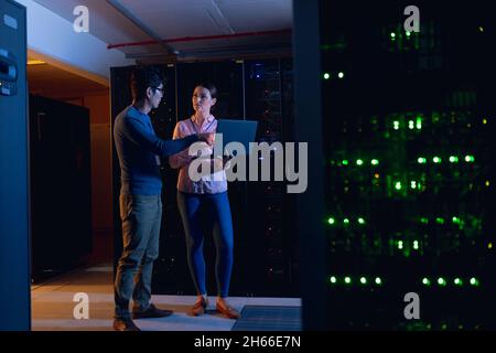 Diverse male and female engineers using laptop in computer server room Stock Photo