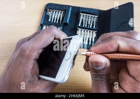 Asian adult male hands trying to open an iPhone using Philips screw driver set with a table background. self-service repair Stock Photo