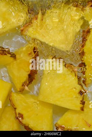 Close up view of the yellow pineapple slices in lemonade background. Texture of cooling sweet summer's drink with macro bubbles on the white backgroun Stock Photo